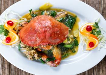 High angled view of a freshly cooked whole Dungeness crab in green onion sauce on white plate.