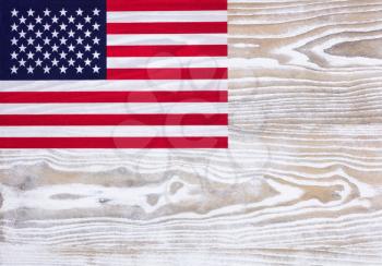 Overhead view of a United of America flag, upper left hand corner on faded white wood. 