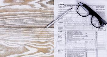 Overhead view of tax form, pen, and reading glasses on fading white desktop. 