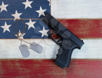 Pistol and military identification tags on top of faded USA flag colors of red, white, and blue on aging boards. Patriotic concept with gun rights. 