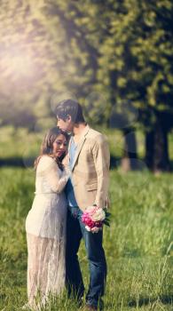Expecting mom and dad, with flowers, holding each other in open grassy field. Haze light effect applied to image.    