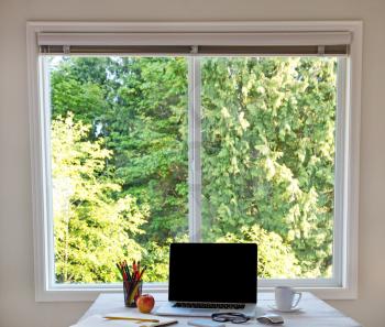 Organized desktop in front of large window with bright daylight and trees in background