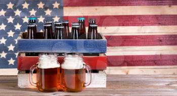 Two pint jars filled with beer, crate with unopen bottle and vintage wooden USA flag in background. Holiday party concept. 