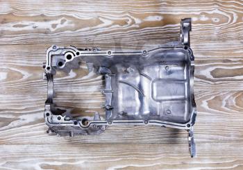 Overhead view of the inside of a defected aluminum car engine oil pan on rustic white boards.