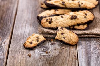Close up of chocolate chip cookies on linen napkin with rustic wood. Selective focus on broken cookies in forefront of image.