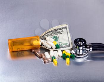 Medical cost concept with pills, bottle, stethoscope, and paper currency on stainless steel table. 