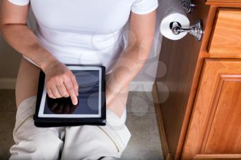 Partial view of a women using wireless internet device while sitting on the toilet. Selective focus on her index finger. 