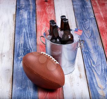 Top view of American football and bucket of ice cold beer on rustic wooden boards painted in USA national colors.
