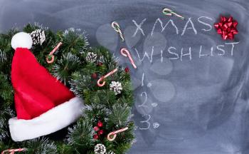 Wreath, Santa cap, gift bow and candy canes on erased chalkboard with Christmas wish list written on board. 