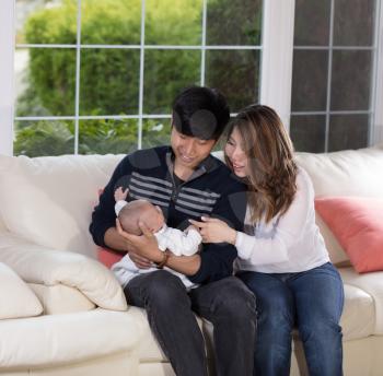 Happy mother and father holding young baby boy on family sofa