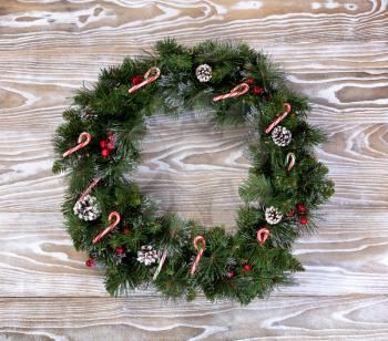 Evergreen Christmas wreath with lights, pine cones and candy canes on white wood. 