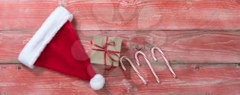 Rustic red wooden background for Christmas concept with gift box, Santa cap and candy canes. Overhead view with copy space.