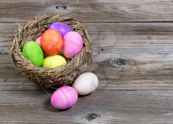 Close up front view of colorful Easter eggs in bird nest on rustic wooden boards. 