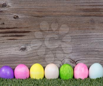 Colorful Easter egg decorations on grass with rustic wood in background. 