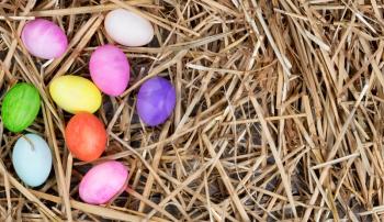 Colorful Easter egg decorations forming left hand border on natural straw and wood. 