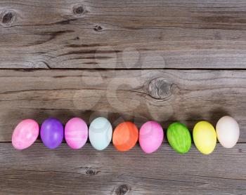Colorful Easter egg decorations forming lower border on rustic wood. 