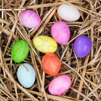 Colorful Easter egg decorations on natural straw and wood. Overhead view. 