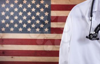 Closeup of medical doctor jacket with stethoscope against faded boards painted in USA flag background. Healthcare concept for America.  