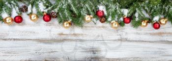 Christmas evergreen branches with golden and red ornaments on rustic white wood background