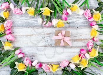 Assortment of spring flowers forming heart shape with boxed gift on white rustic wooden boards 