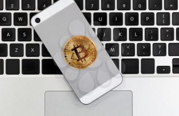 Bitcoin currency on smart phone with computer keyboard in background.  Crypto investment via wireless mobile technology concept