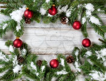 Christmas snowy tree branches and red ornaments forming circular border on rustic white wood