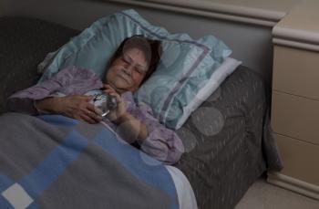 Restless senior woman tightly holding her alarm clock during nighttime