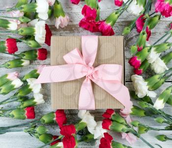 Colorful carnations surrounding gift box on white weathered wooden boards 