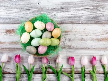 colorful tulips and basket filled with eggs forming lower border on rustic white wood for Easter Background 