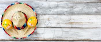 Overhead view of traditional maracas on top of a large sombrero for Cinco de Mayo holiday celebration on weathered white wooden boards