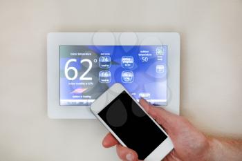Male hand holding smart phone to operate heating or cooling of thermostat for home