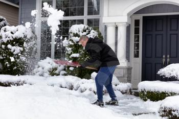 Mature man shoveling snow in front of home sidewalk  