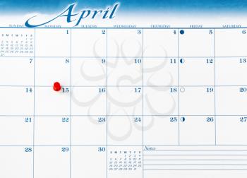 Red pushpin on day of April 15 of calendar for tax income due date reminder in overhead view