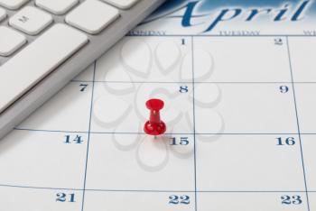 Red pushpin on day of April 15 of calendar for tax income due date reminder