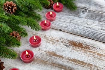 Traditional Christmas holiday candles and evergreen branches with on white rustic wood background 