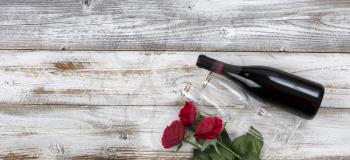 Happy Valentines Day celebration with red roses, drinking glasses and a bottle of wine on white rustic wooden background   
