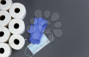Supplies like toilet paper, mask and gloves for surviving against COVID-19 or Coronavirus on gray background. 