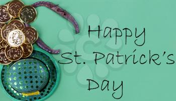 St Patricks day Irish elf hat, horse shoe and gold coins on a green paper background with copy space plus text message