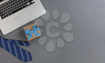 Fathers day concept with blue dress tie, gift box and laptop computer on a gray background in flat lay format