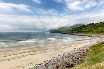 Natural beach of Ireland in the Atlantic Ocean with farm pastures and mountains in background 