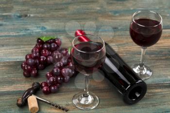 Selective focus of rim of red wine glass with bottle, grapes and vintage corkscrew on faded blue wood planks in background 