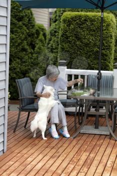 Senior woman enjoying the company of her pet dog while preparing herbs outside on the home deck  