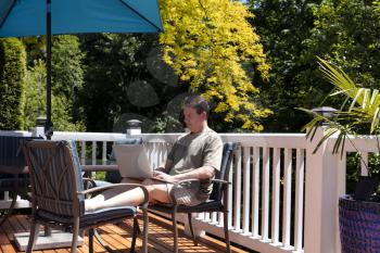 Mature man working remotely from home outdoor deck during nice day   