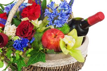 Flower arrangement of roses, orchids, fruits and bottle of wine in basket isolated on white background. Closeup.