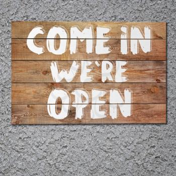 Vintage Come in we are open wooden sign on gray stucco concrete wall.