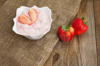 Fresh juicy strawberry with yogurt in white bowl on wooden background. Closeup.