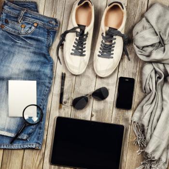 Set of travel items including scarf, sunglasses, sneakers, note book, magnifying glass, map, mobile phone and jeans. Different travel objects and passenger luggage on grey wooden background. Top aeria