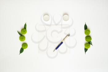 Paper, pen and candles with decoration of chrysanthemum flowers and ficus leaves on white background. Overhead view. Flat lay.