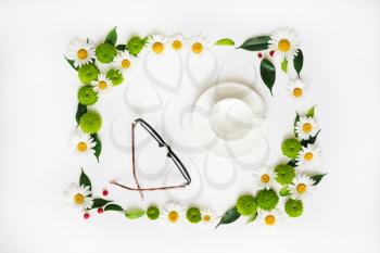 Cup for coffee or tea and glasses with wreath frame from chamomile and chrysanthemum flowers, ficus leaves and ripe rowan on white background. Overhead view. Flat lay.