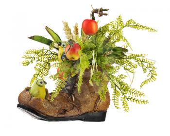Table floral arrangement made of artificial flowers and fruits in stylized ceramic vase in the form of an old shoe with two birdies, holding in its beak ears of wheat isolated on white background.